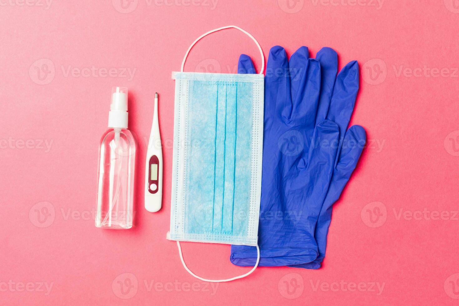 Top view of alcohol hand sanitizer, latex gloves, digital thermometer and medical mask on pink background. Virus protection equipment concept with copy space photo