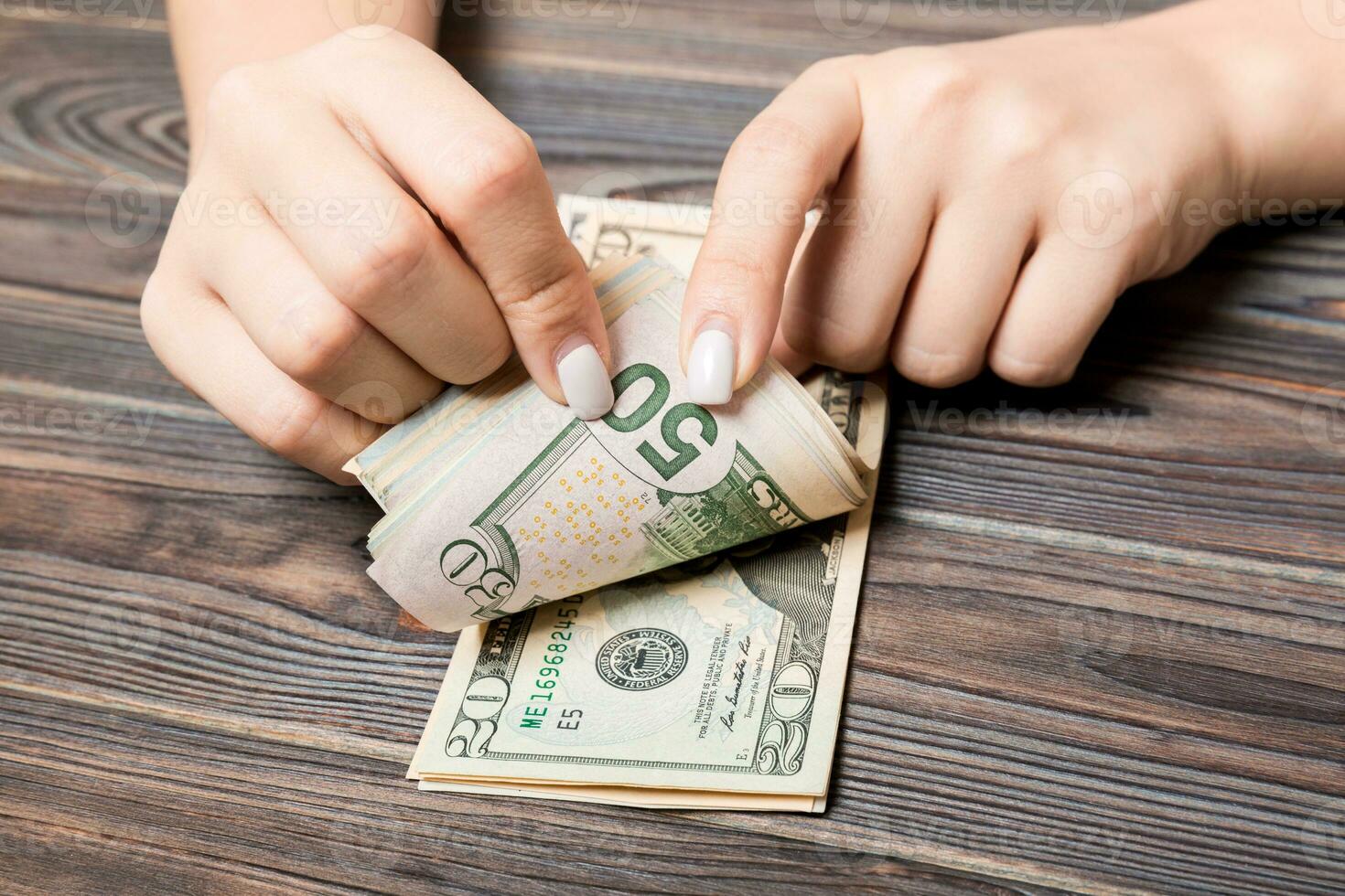 Perspective view of a businesswoman's hands counting fifty and twenty dollar banknotes on wooden background. Success and wealth concept photo
