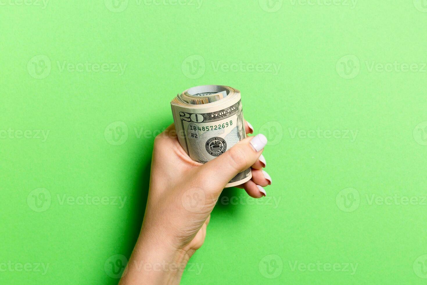 Female hand holding tightly a bundle of money. Top view of twenty dollars on colorful background. Investment concept photo
