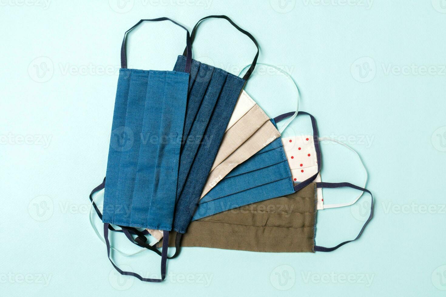 Top view of a pile of homemade textile reusable masks on blue background. Respiratory protection concept with copy space. DIY concept photo