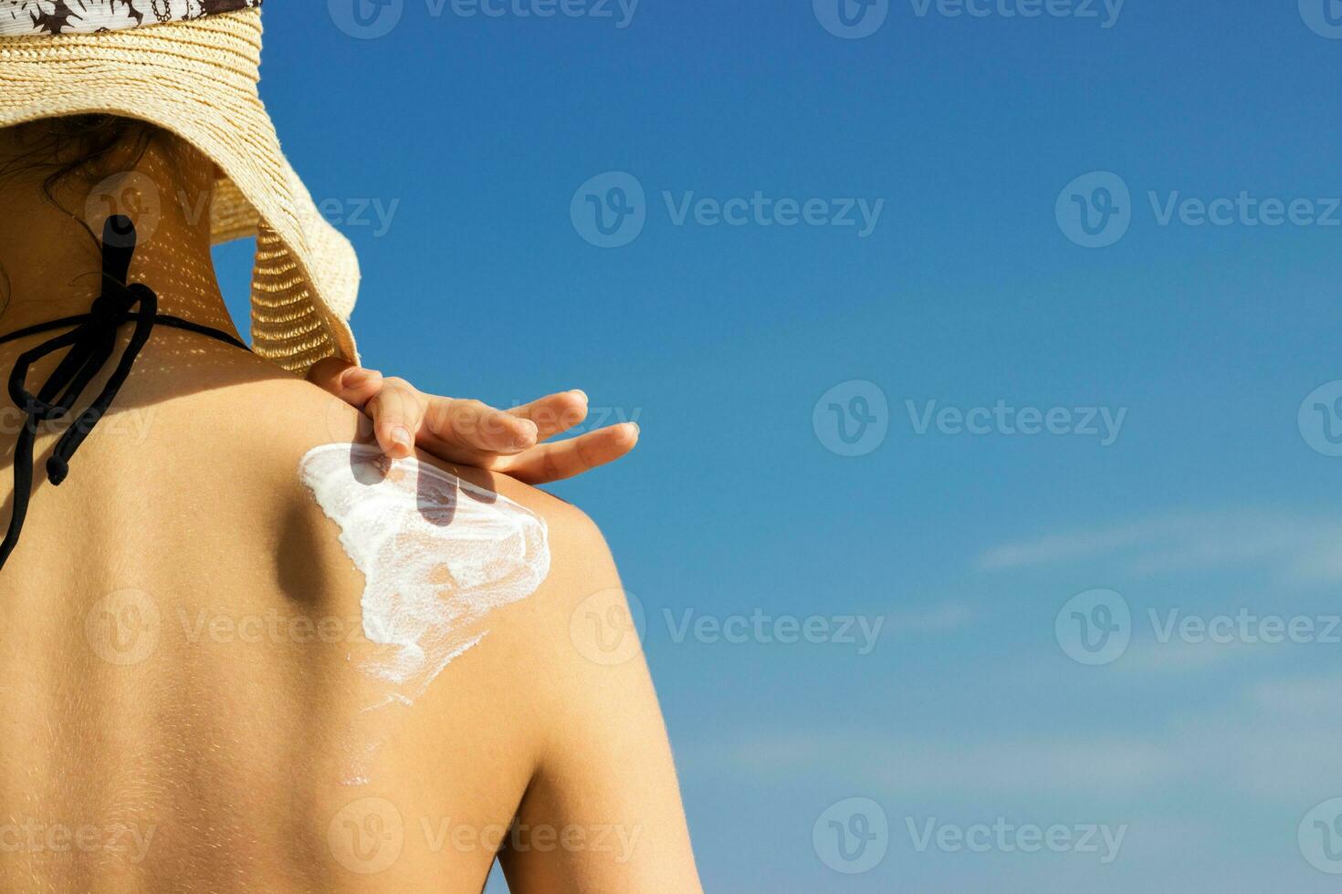 Woman in a hat applying sunscreen on her shoulder photo