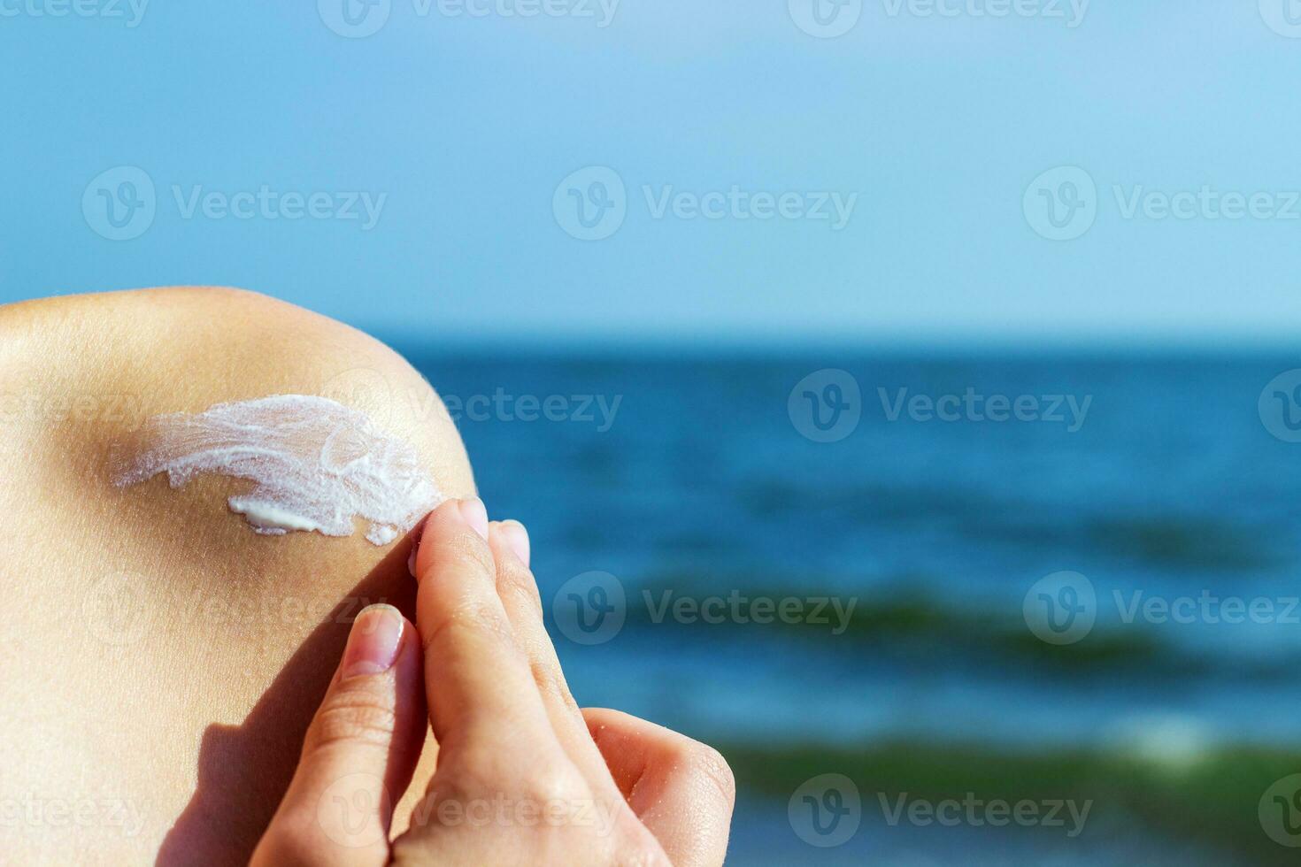 Woman applying sunscreen at the beach on hot summer day. A girl smears a shoulder with sunscreen photo