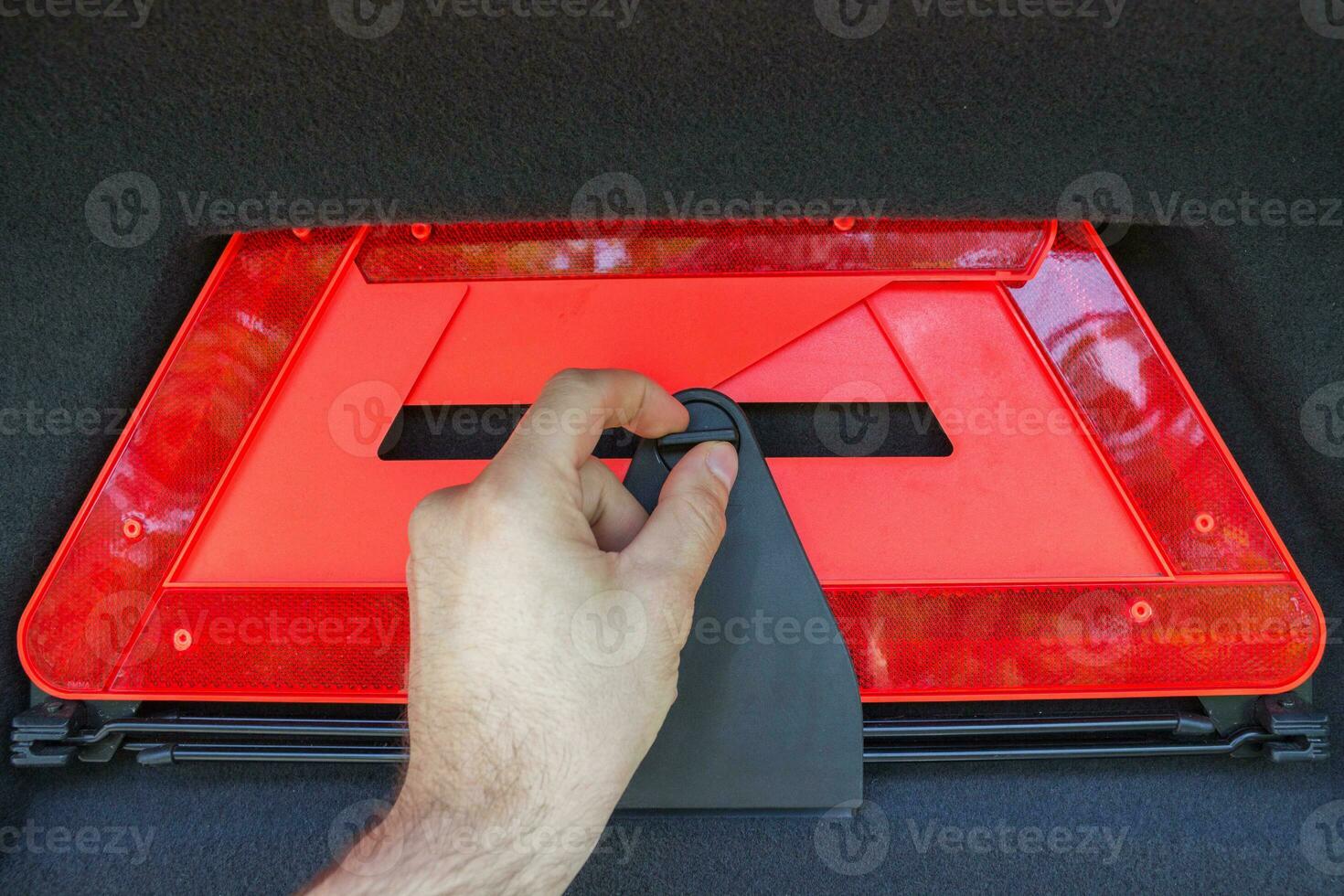 A man hand pulls out a red folded emergency sign lies from the trunk. photo