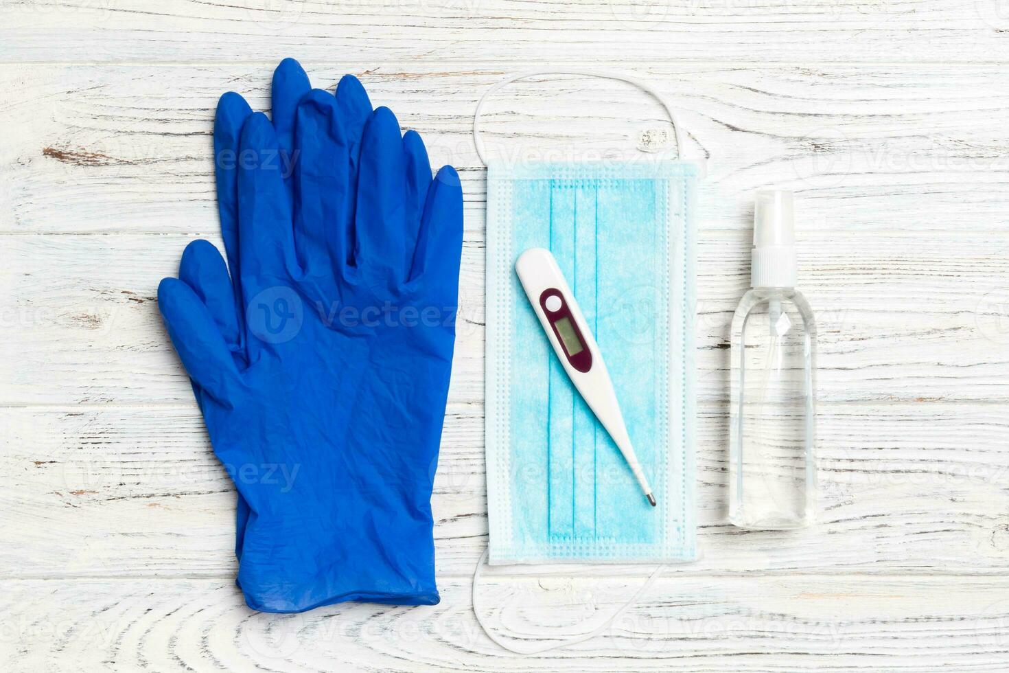 Top view of surgical mask, latex gloves, alcohol hand sanitizer and digital thermometer on wooden background with copy space. Protective medical equipment concept photo