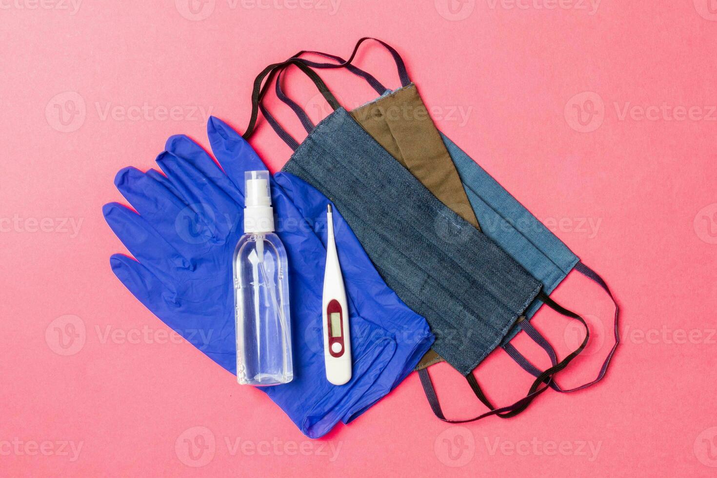 Top view of alcohol hand sanitizer, latex gloves, digital thermometer and handmade reusable masks on pink background. Virus protection equipment concept with copy space photo