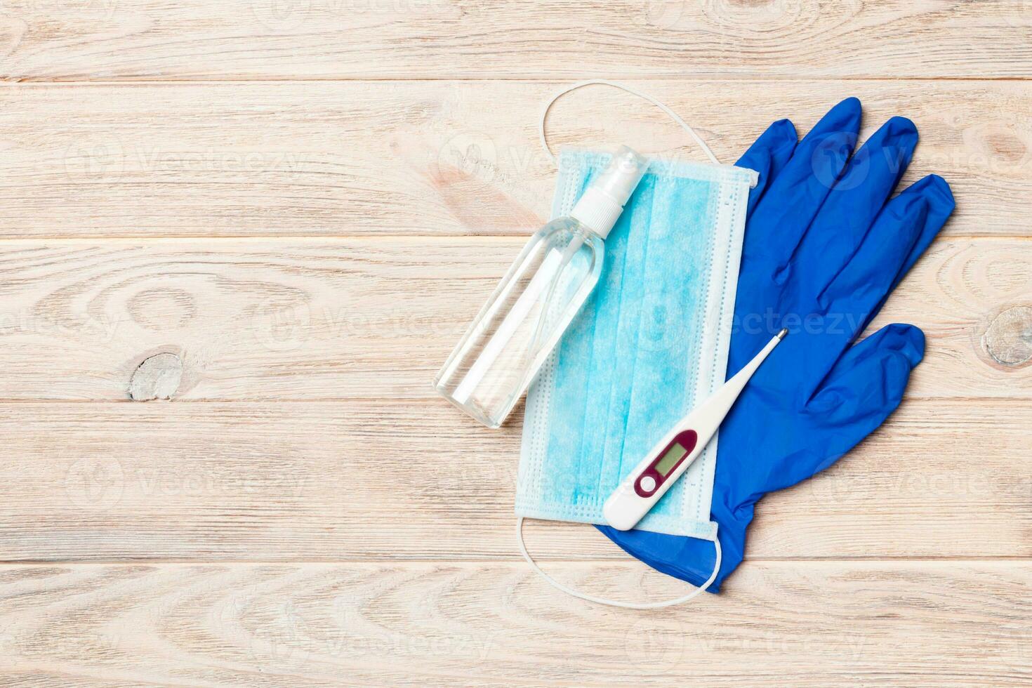 Top view of alcohol hand sanitizer, latex gloves, digital thermometer and surgical mask on wooden background. Virus protection equipment concept with copy space photo