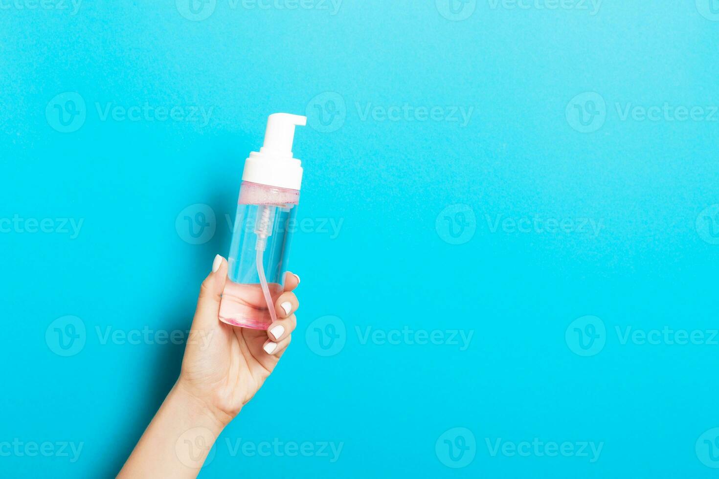 Female hand holding spray cream bottle of lotion isolated. Girl give cosmetic products on blue background photo