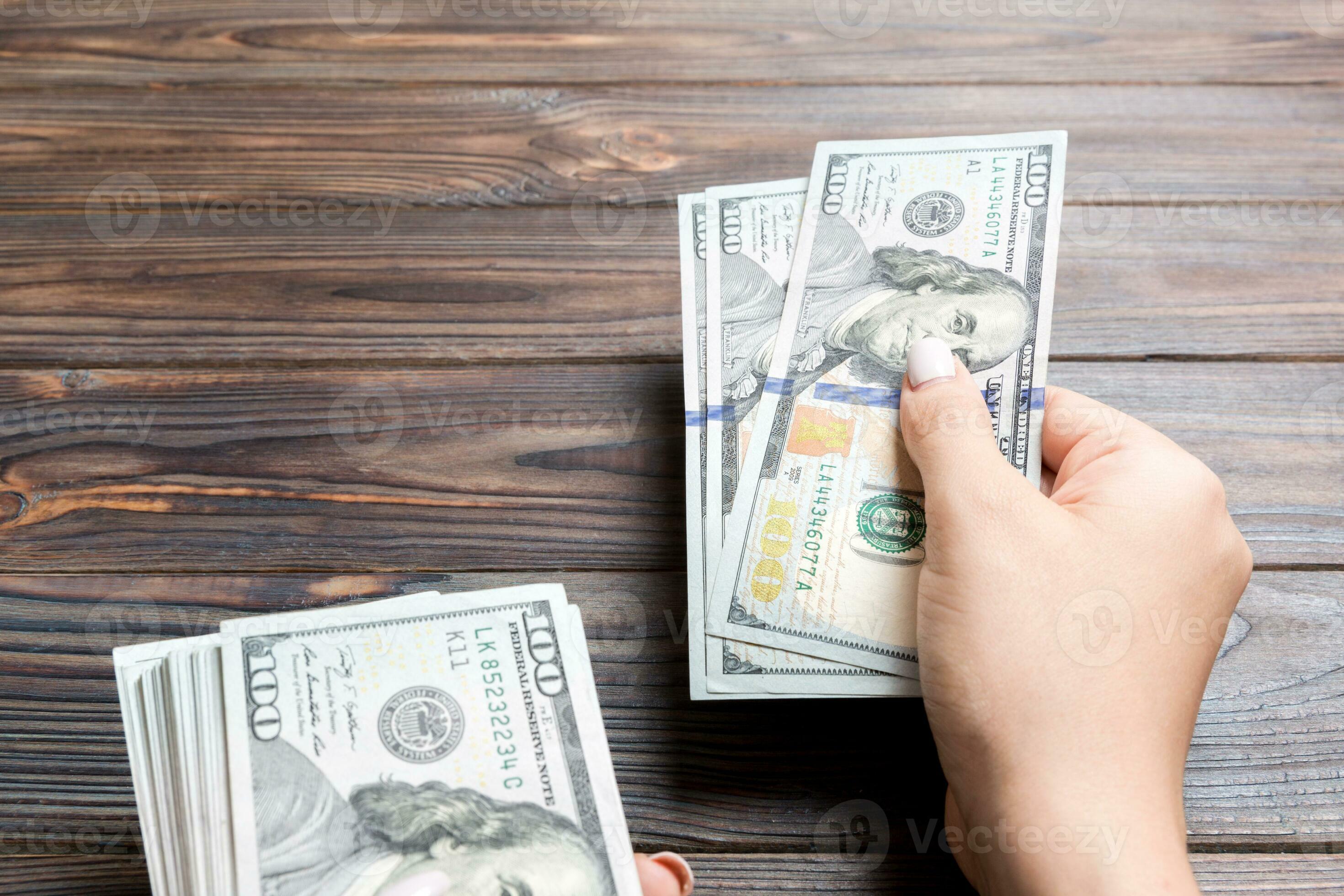 Female Hand Giving One Hundred Dollar Banknotes On Wooden Background female-hand-giving-one-hundred-dollar-banknotes-on-wooden-background