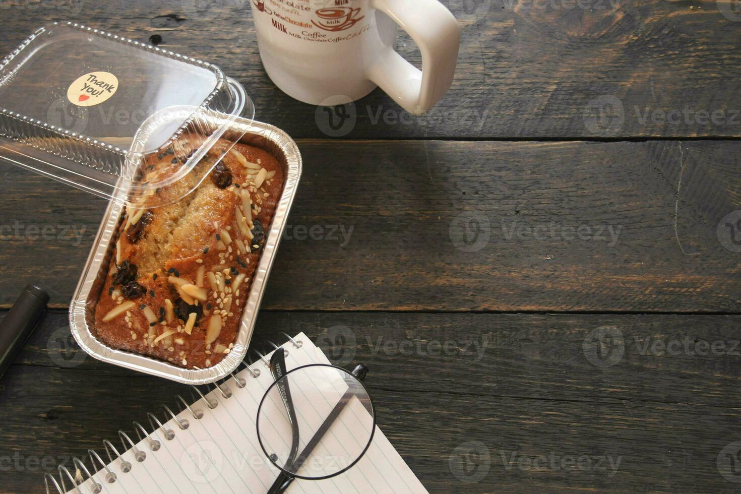 Banana Cake on a black wooden table With note book, glasses, and coffee mugs. photo