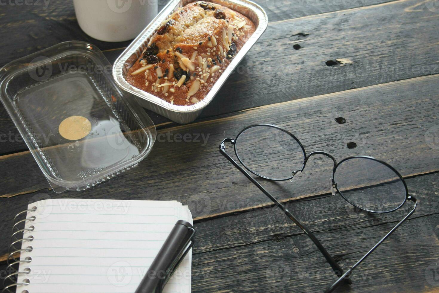 Banana Cake on a black wooden table With note book, glasses, and coffee mugs. photo