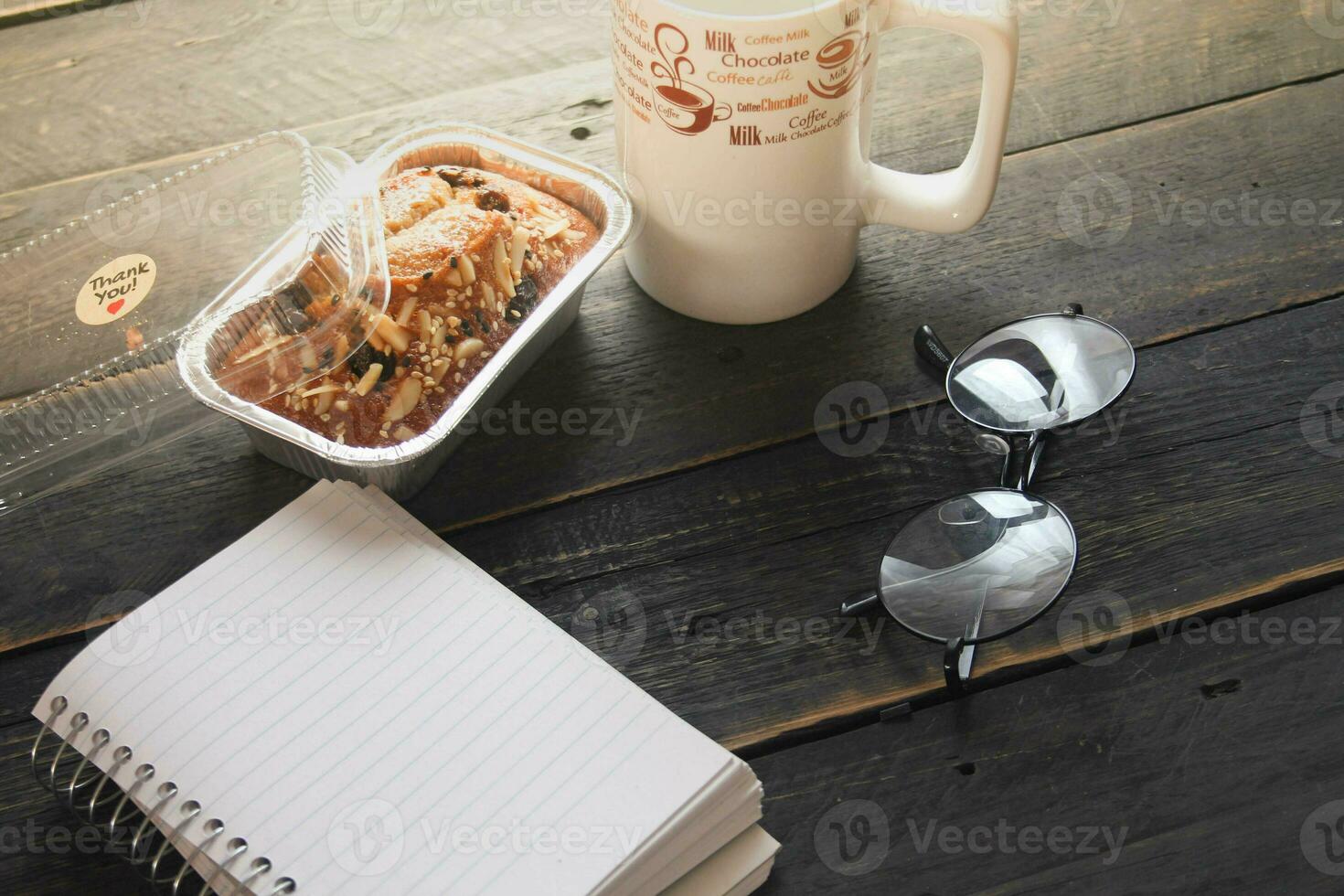 Banana Cake on a black wooden table With note book, glasses, and coffee mugs. photo