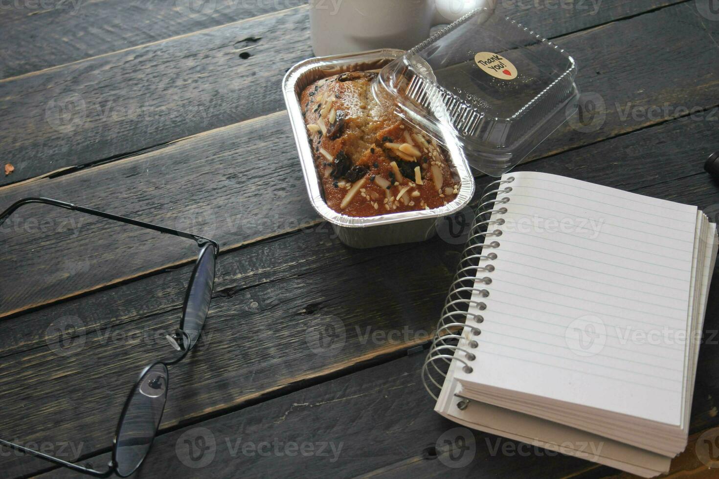 Banana Cake on a black wooden table With note book, glasses, and coffee mugs. photo