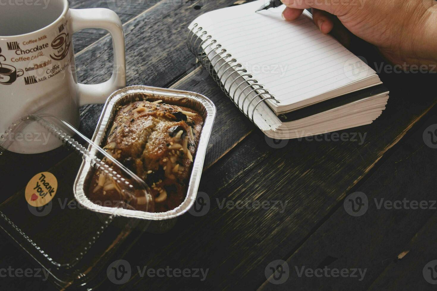 Banana Cake on a black wooden table With note book, glasses, and coffee mugs. photo