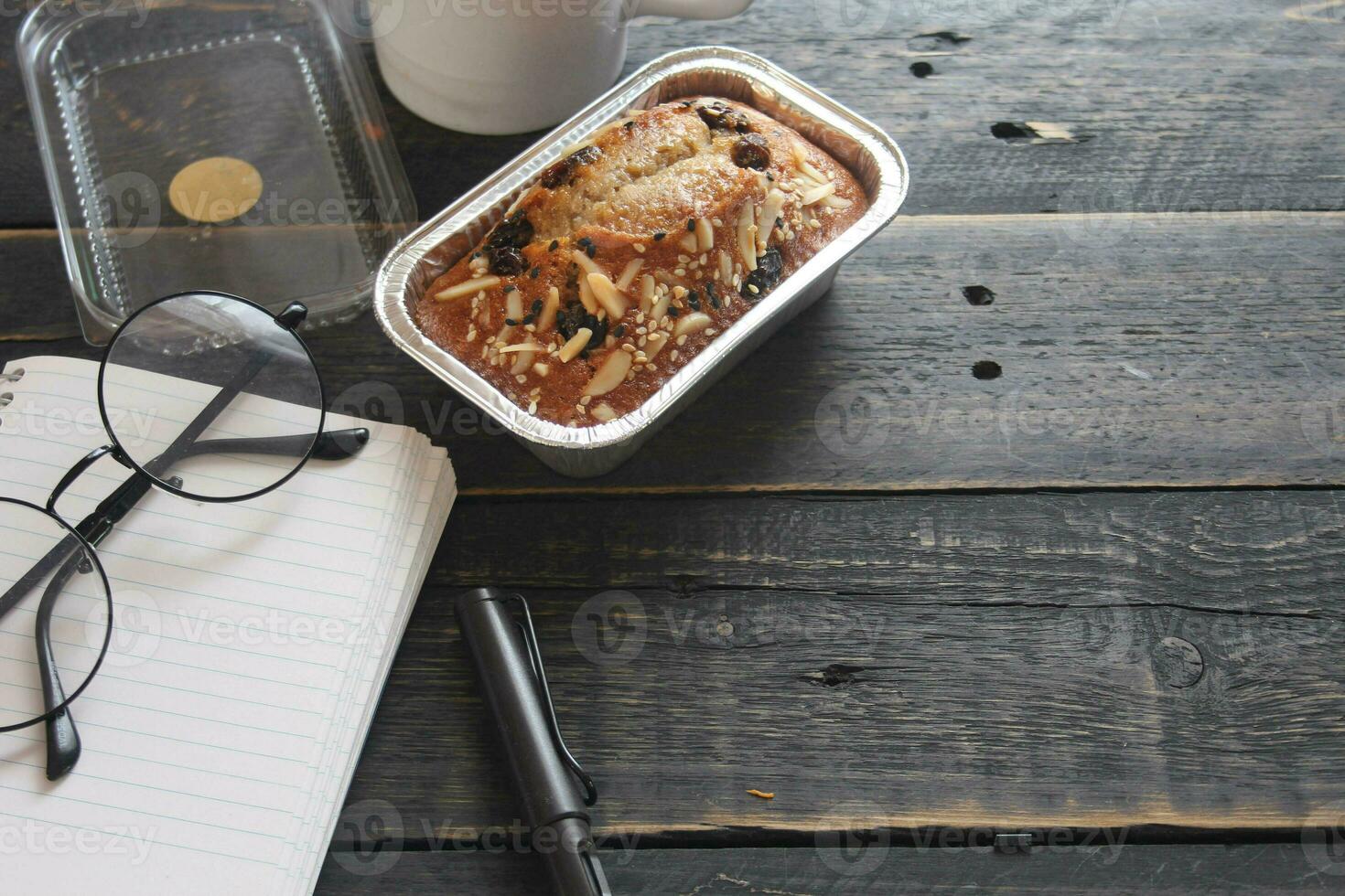 Banana Cake on a black wooden table With note book, glasses, and coffee mugs. photo