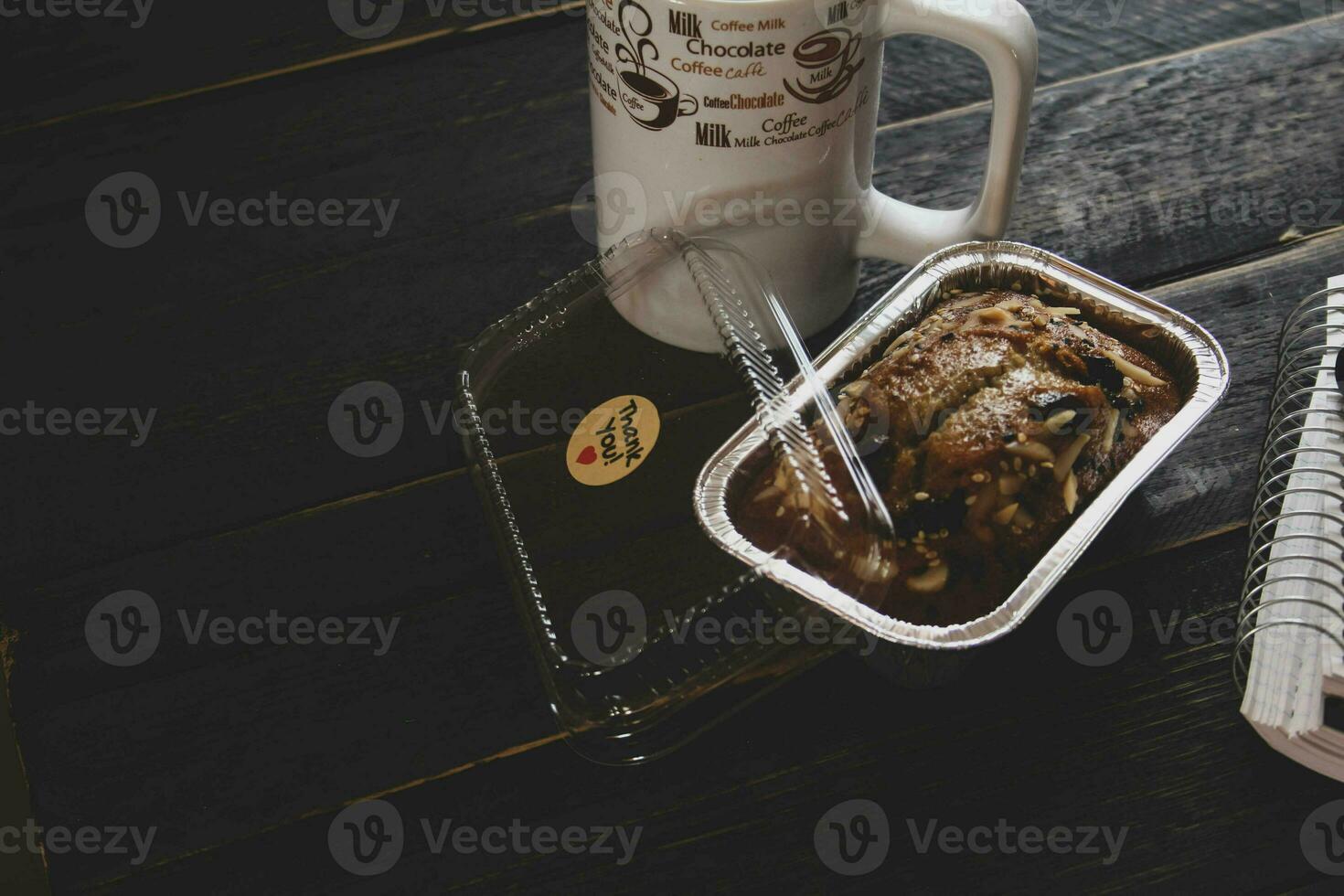 Banana Cake on a black wooden table With note book, glasses, and coffee mugs. photo