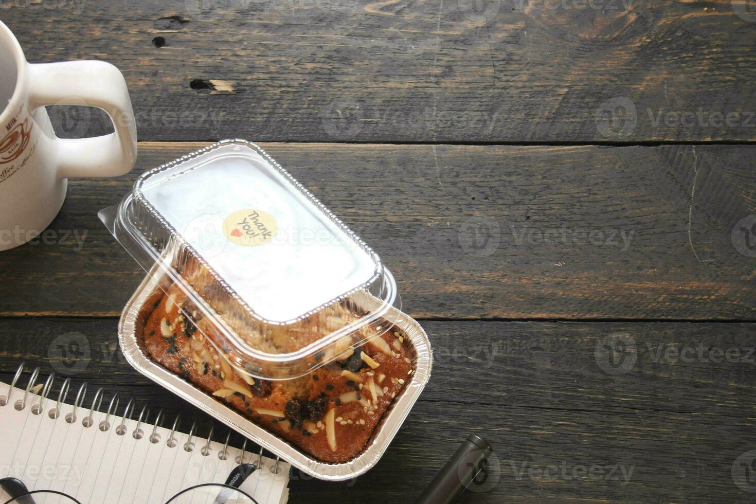 Banana Cake on a black wooden table With note book, glasses, and coffee mugs. photo