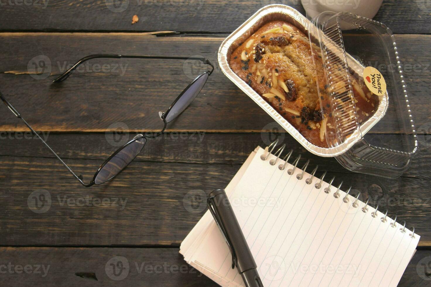 Banana Cake on a black wooden table With note book, glasses, and coffee mugs. photo