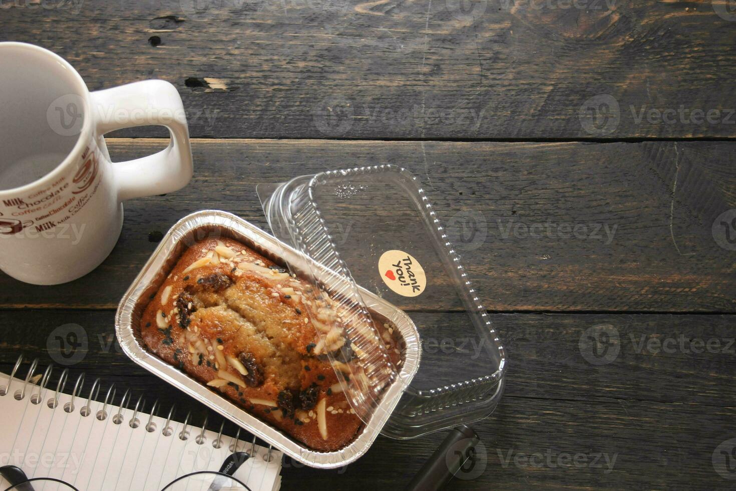 Banana Cake on a black wooden table With note book, glasses, and coffee mugs. photo