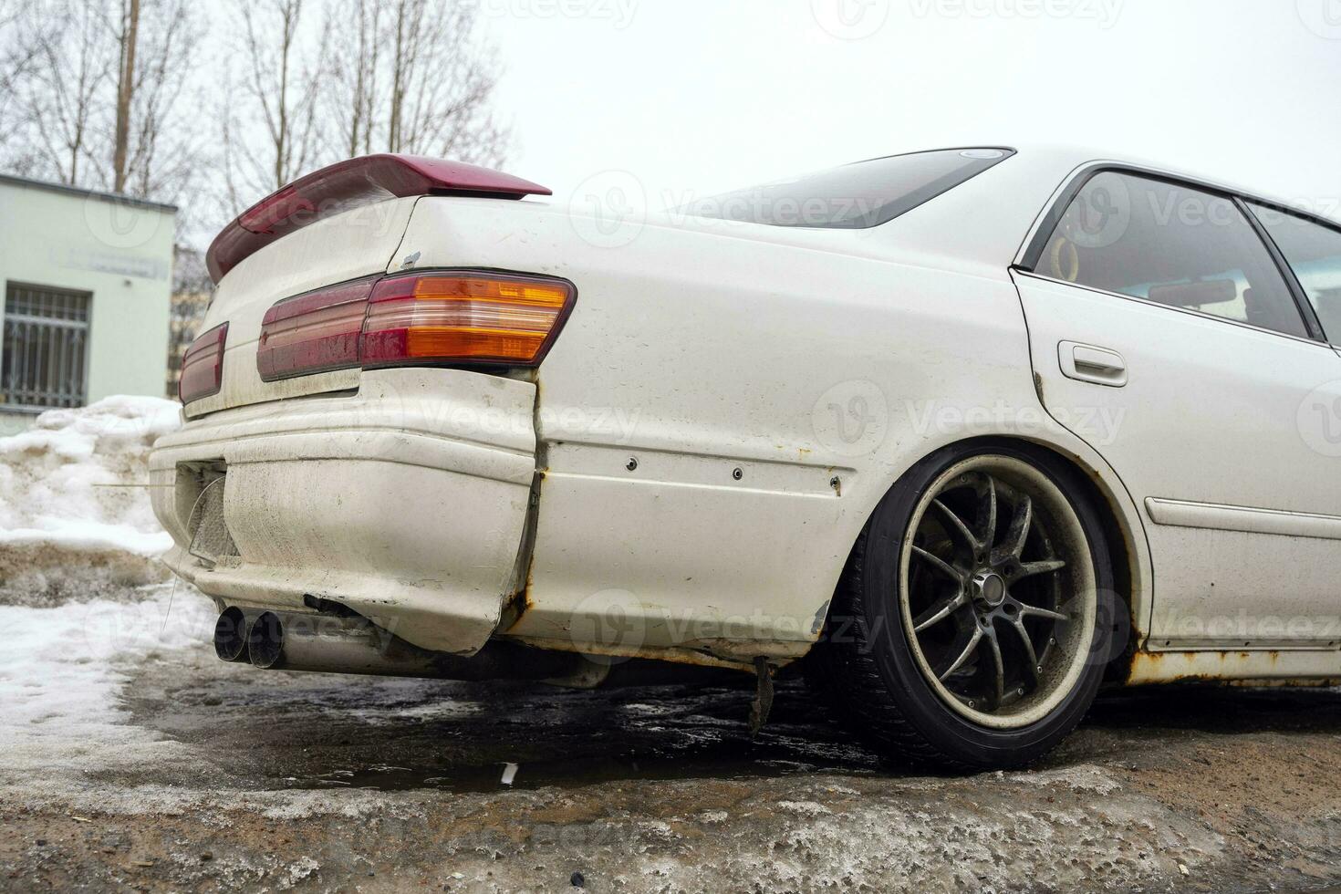 the back of a white smashed Japanese sedan with black rims with a damaged bumper photo