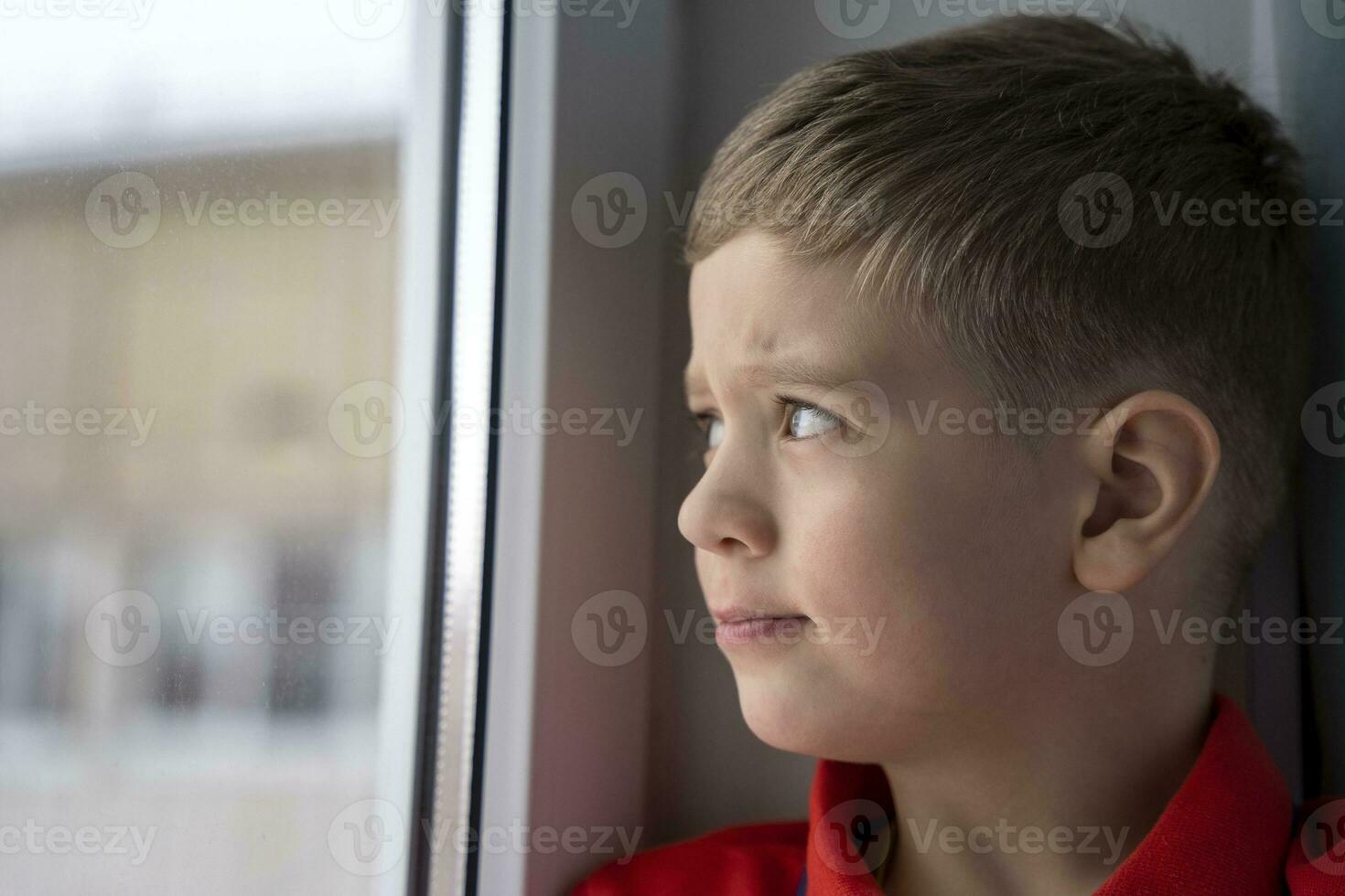 portrait of a charming little Caucasian boy who looks out the window sitting at home photo