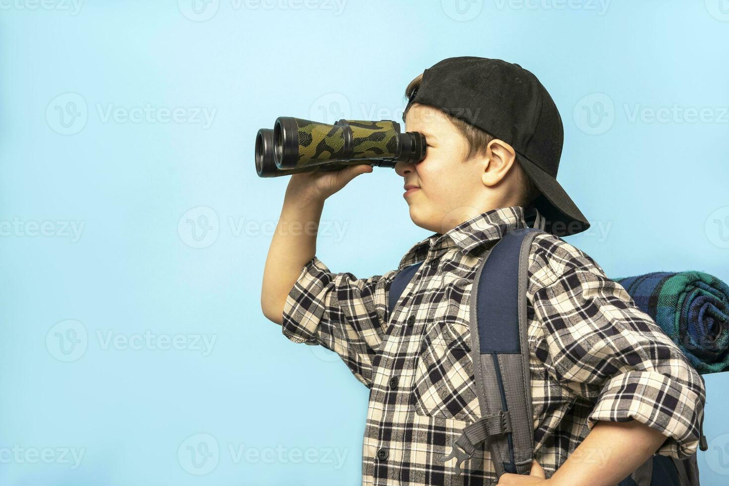 boy tourist looks through binoculars on a blue background, copy space photo