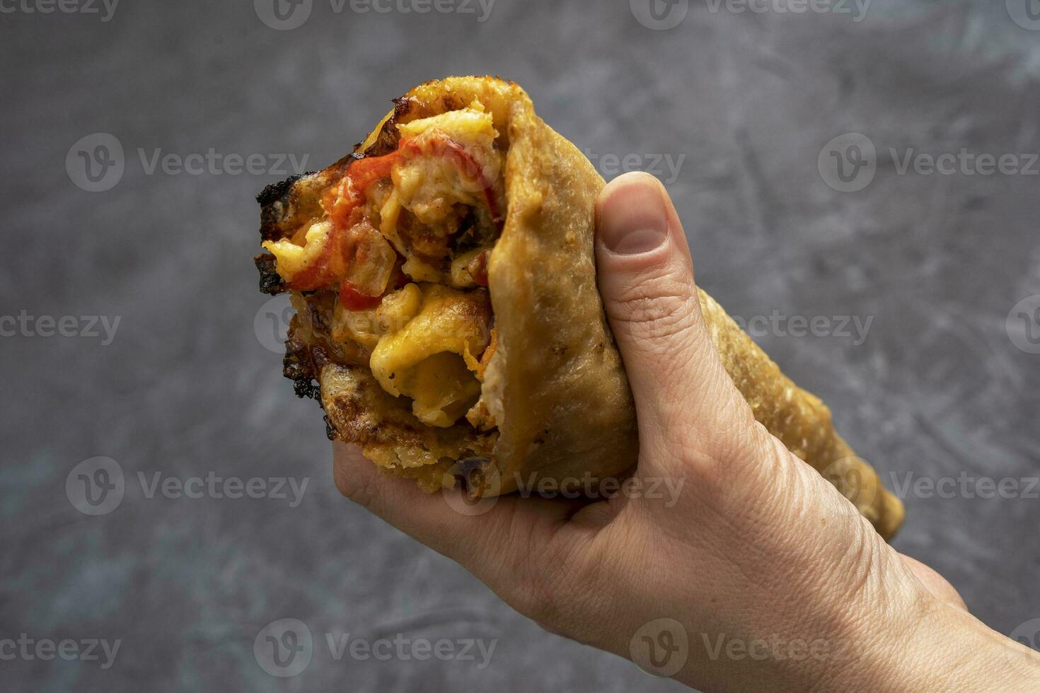 Pizza cone in a woman's hand on a dark gray background. Fast Food Delicious pizza cone with crispy thin crust, photo