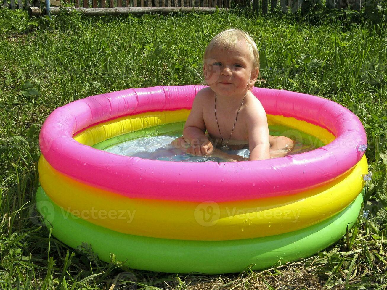 niño es sentado en un vistoso inflable piscina con agua en verano foto