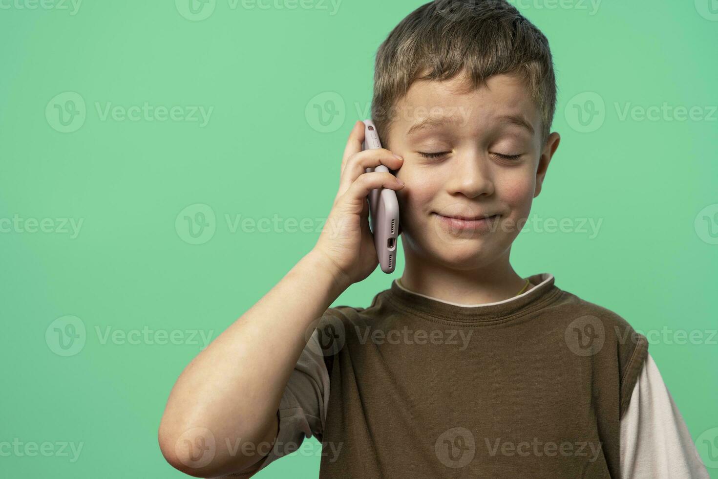 funny Caucasian boy is talking on the phone with his eyes closed with pleasure photo