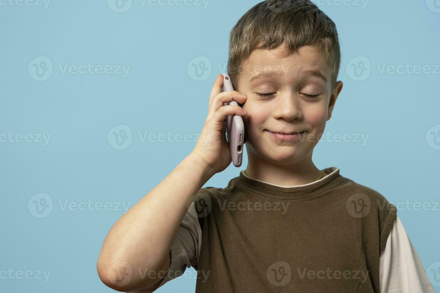 funny Caucasian boy is talking on the phone with his eyes closed with pleasure photo