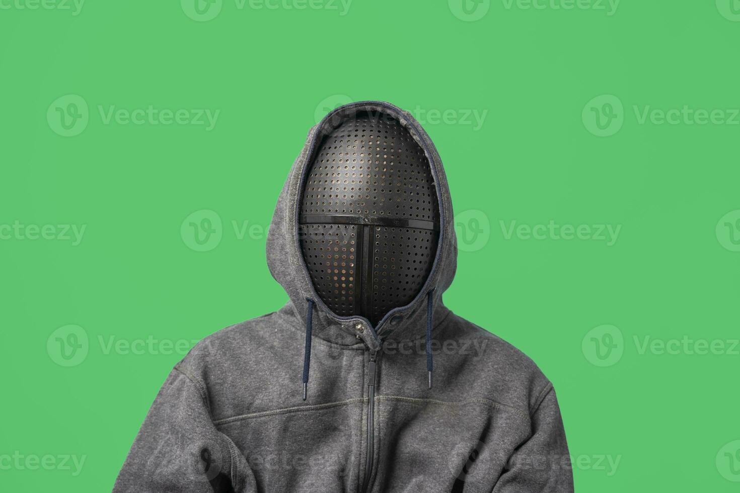 an unrecognizable man in a gray hoodie with a mask on his face isolated on a green background photo