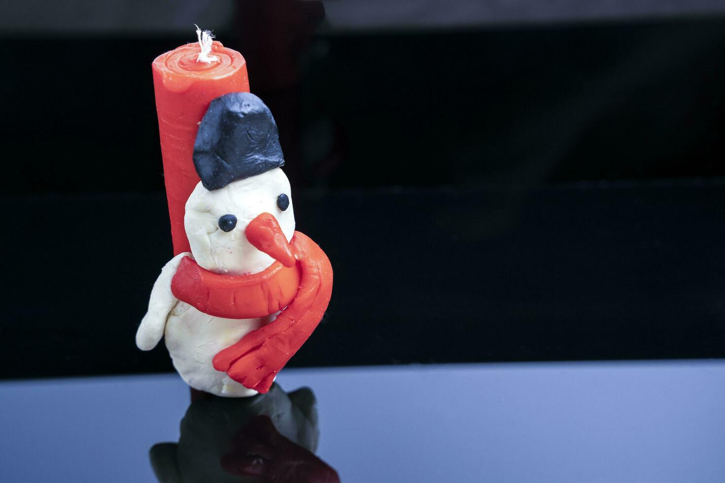 homemade children's candle in the form of a snowman on a glossy black glass background photo