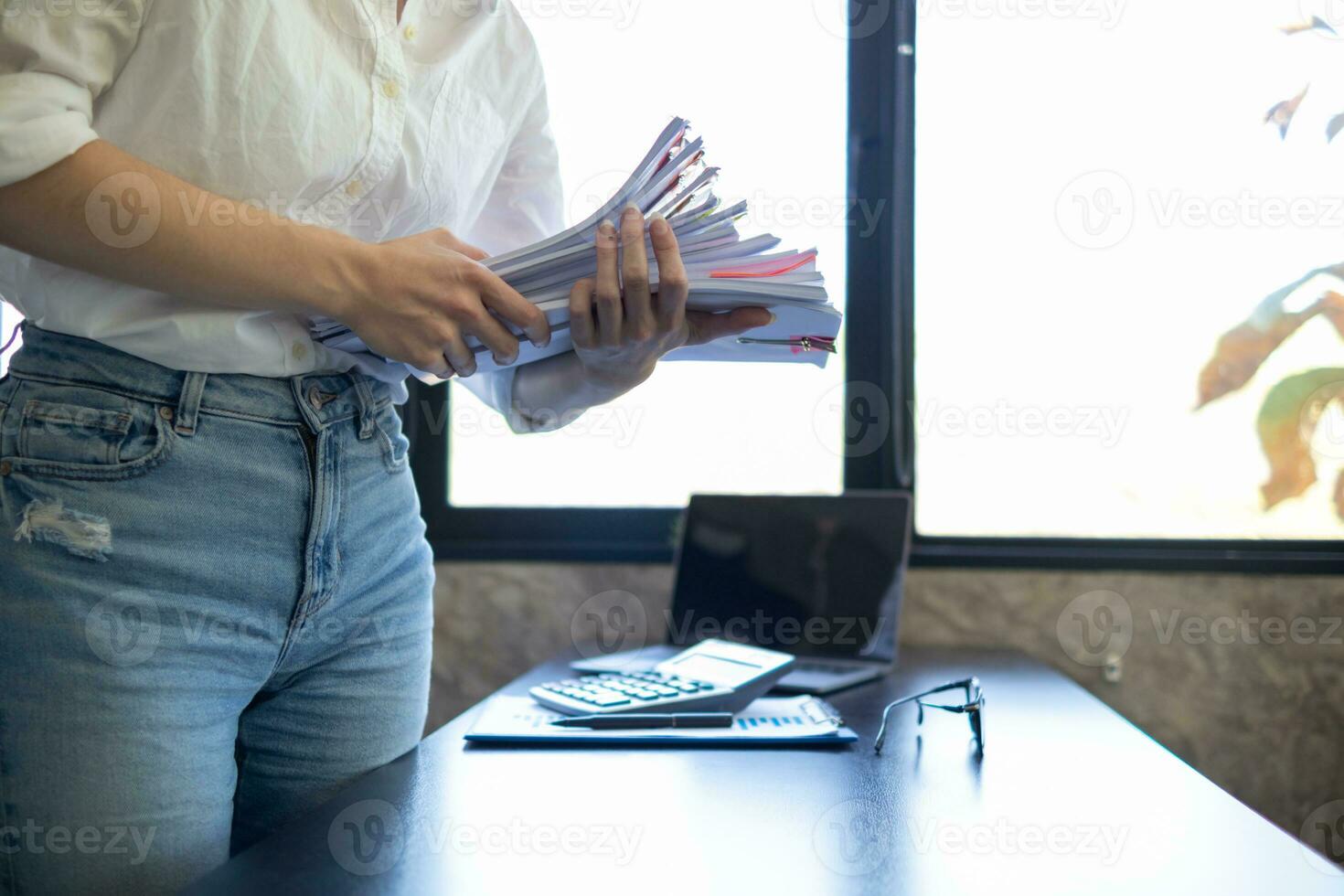 mujer de negocios manos trabajando en pilas de papel documentos a buscar y revisión documentos apilado en mesa antes de enviando ellos a tablero de directores a utilizar correcto documentos en reunión con empresario foto