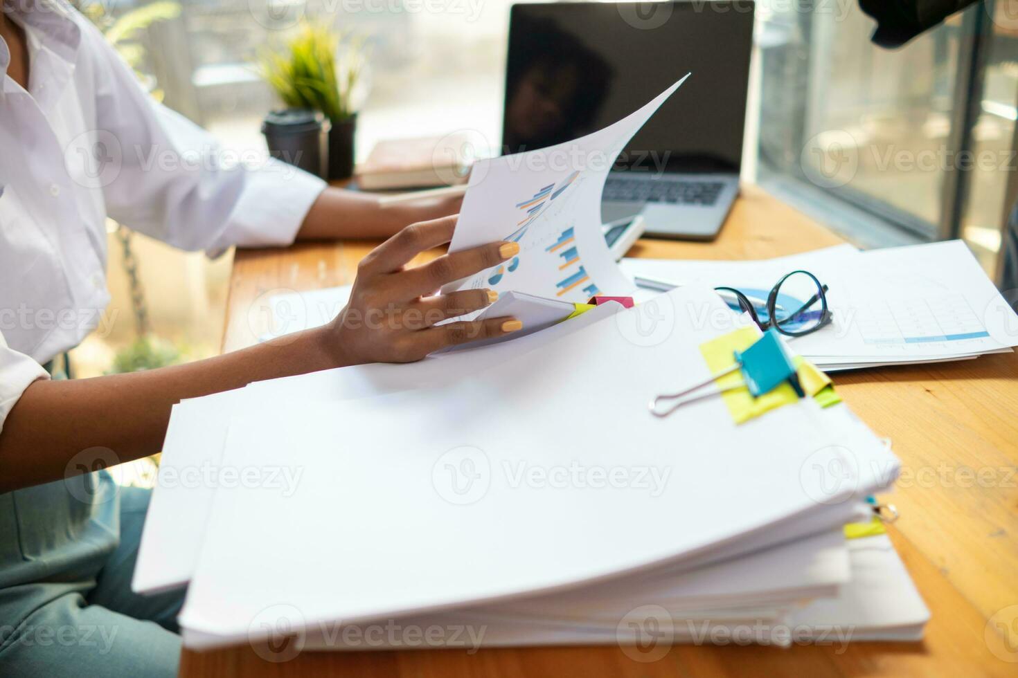 mujer de negocios manos trabajando en pilas de papel documentos a buscar y revisión documentos apilado en mesa antes de enviando ellos a tablero de directores a utilizar correcto documentos en reunión con empresario foto