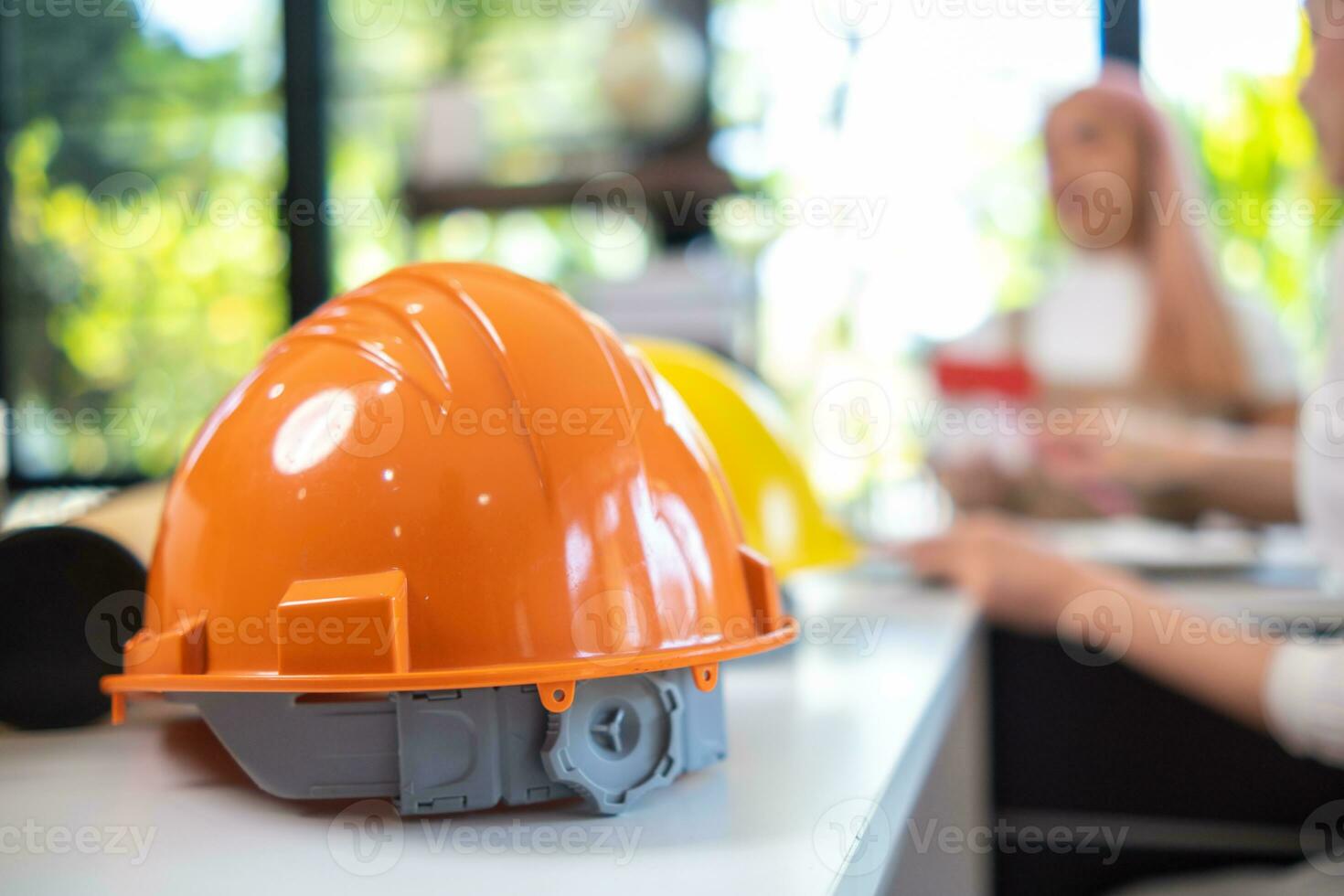 orange hard hats sit on construction engineers desks because hard hats are essential when entering construction site for the safety of engineers.  concept of wearing hard hat to protect head in site. photo