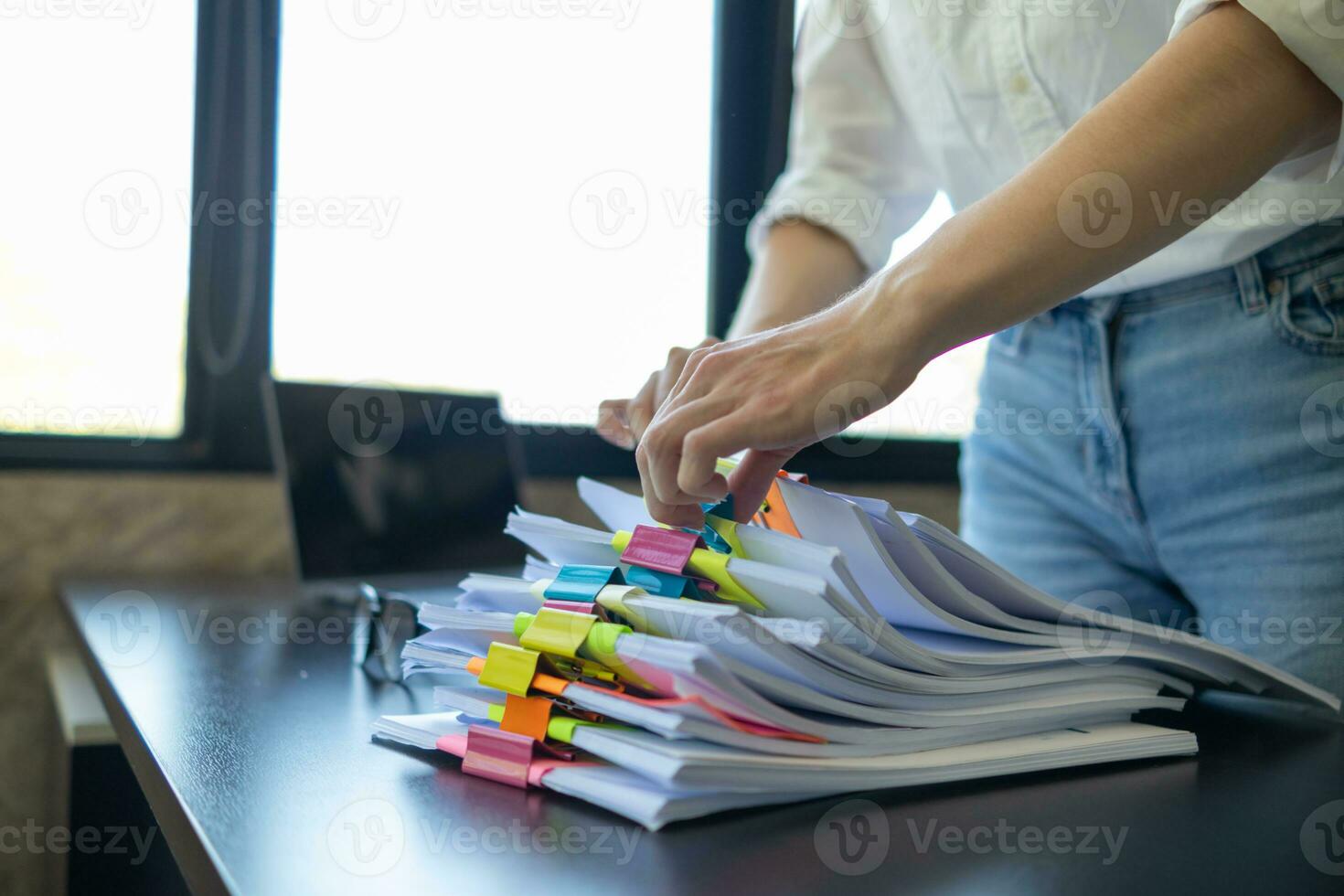 mujer de negocios manos trabajando en pilas de papel documentos a buscar y revisión documentos apilado en mesa antes de enviando ellos a tablero de directores a utilizar correcto documentos en reunión con empresario foto