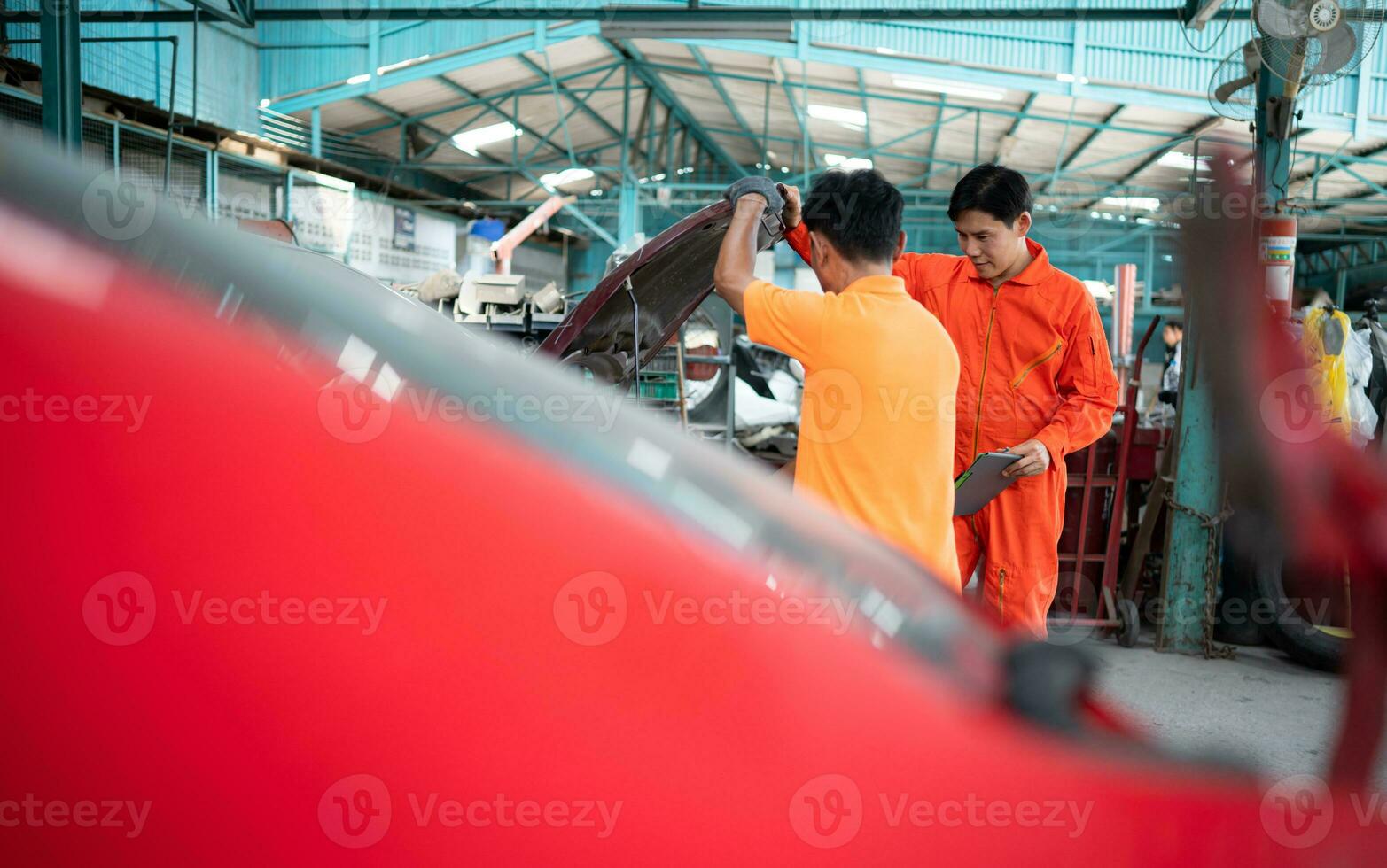 Both of auto mechanics are inspecting the engine of a customer's car being brought in for repair at a garage. photo