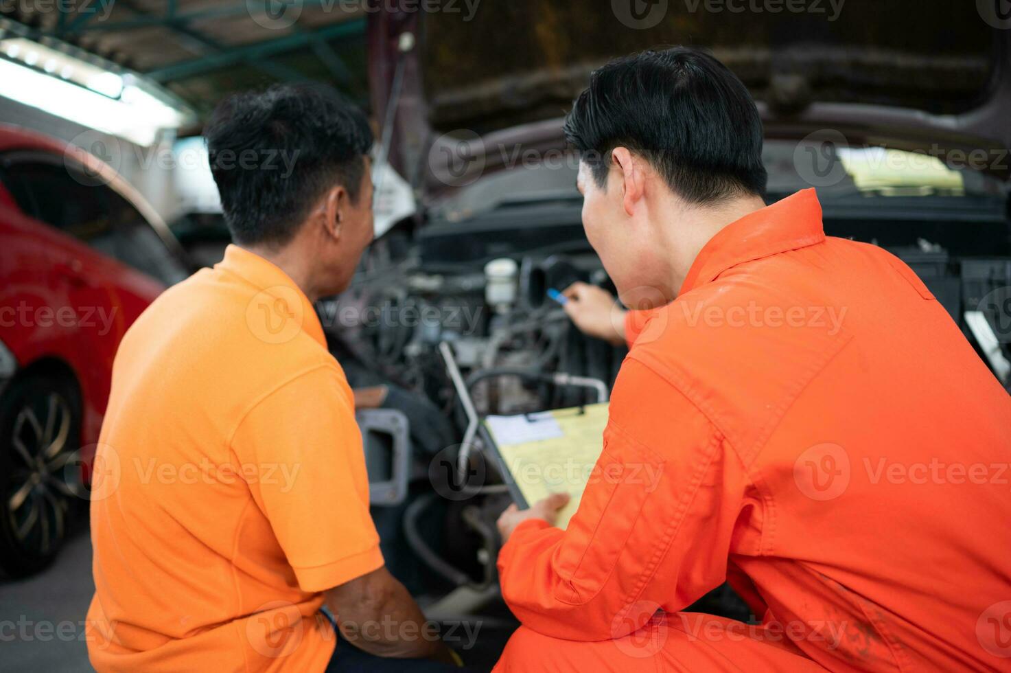 Both of auto mechanics are inspecting the engine of a customer's car being brought in for repair at a garage. photo