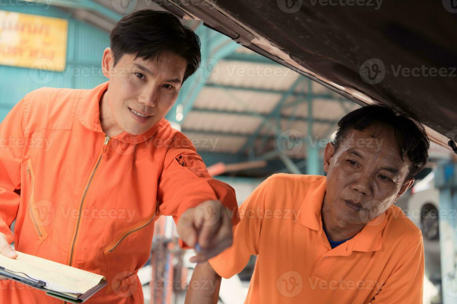 Both of auto mechanics are inspecting the engine of a customer's car being brought in for repair at a garage. photo