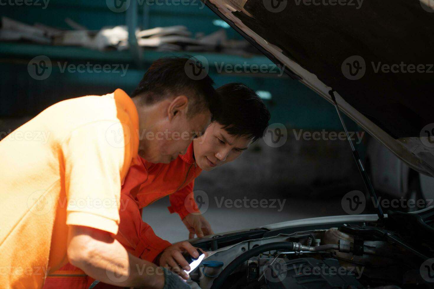 Both of auto mechanics are inspecting the engine of a customer's car being brought in for repair at a garage. photo