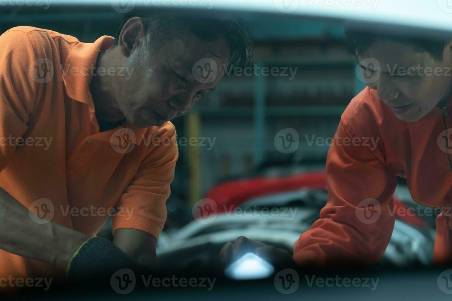 Both of auto mechanics are inspecting the engine of a customer's car being brought in for repair at a garage. photo