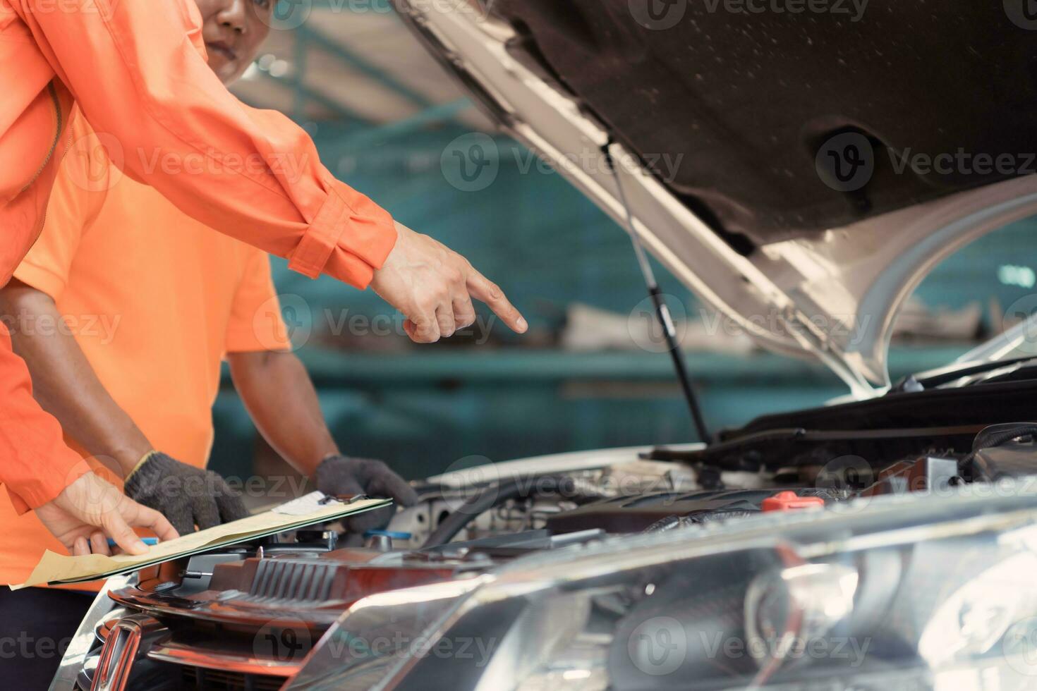 Both of auto mechanics are inspecting the engine of a customer's car being brought in for repair at a garage. photo