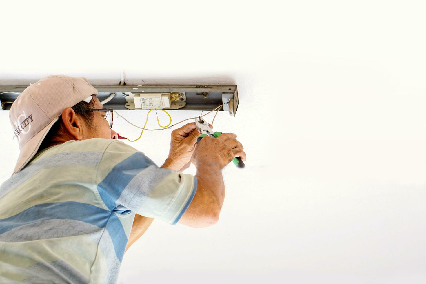 Lampang, Thailand, 2018 - Closeup and look up view of electric repair technician holding pliers and fixing the fluorescent lamp on white building ceiling. photo