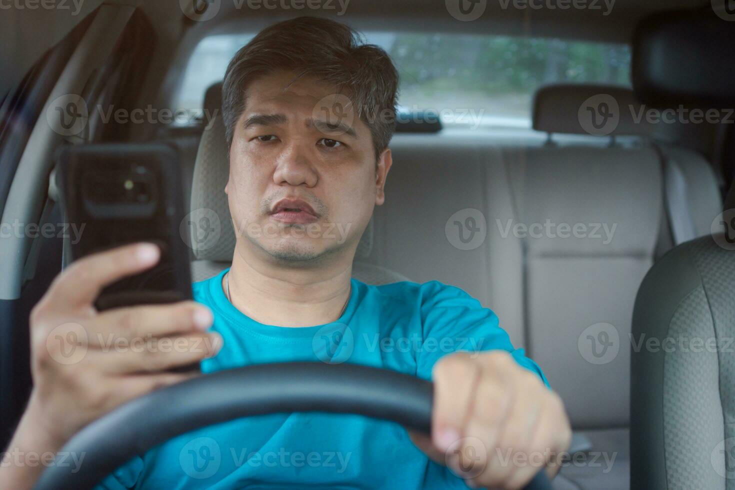 Asian man using mobile smart phone and reading messages while driving a car. Concept of negligence, dangerous behavior and accident risk photo