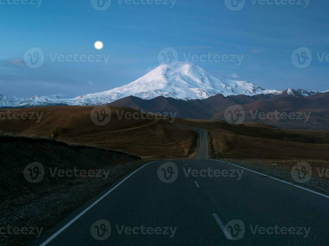 Morning landscape with winding highway to Mount Elbrus under morning sky with full moon. Empty road disappear into the distance at twilight. Way with markup perspective view. Kabardino-Balkaria. photo