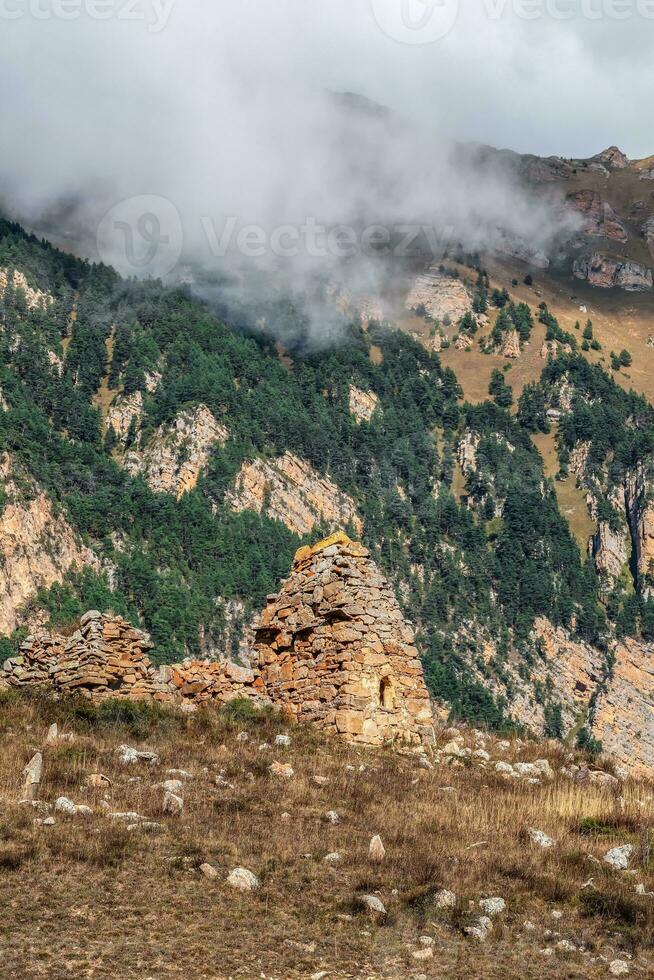 Old family crypt. Beautiful dramatic landscape nature view in the mountains. Old Ossetian battle tower in the misty mountains. Digoria region. North Ossetia, Russia. Vertical view. photo