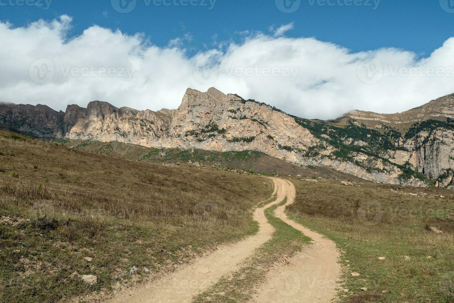 Old path through mountains. Trekking mountain trail. Bright atmospheric minimalist alpine landscape with stony footpath among grasses in highlands. Pathway uphill. Way up mountainside. photo