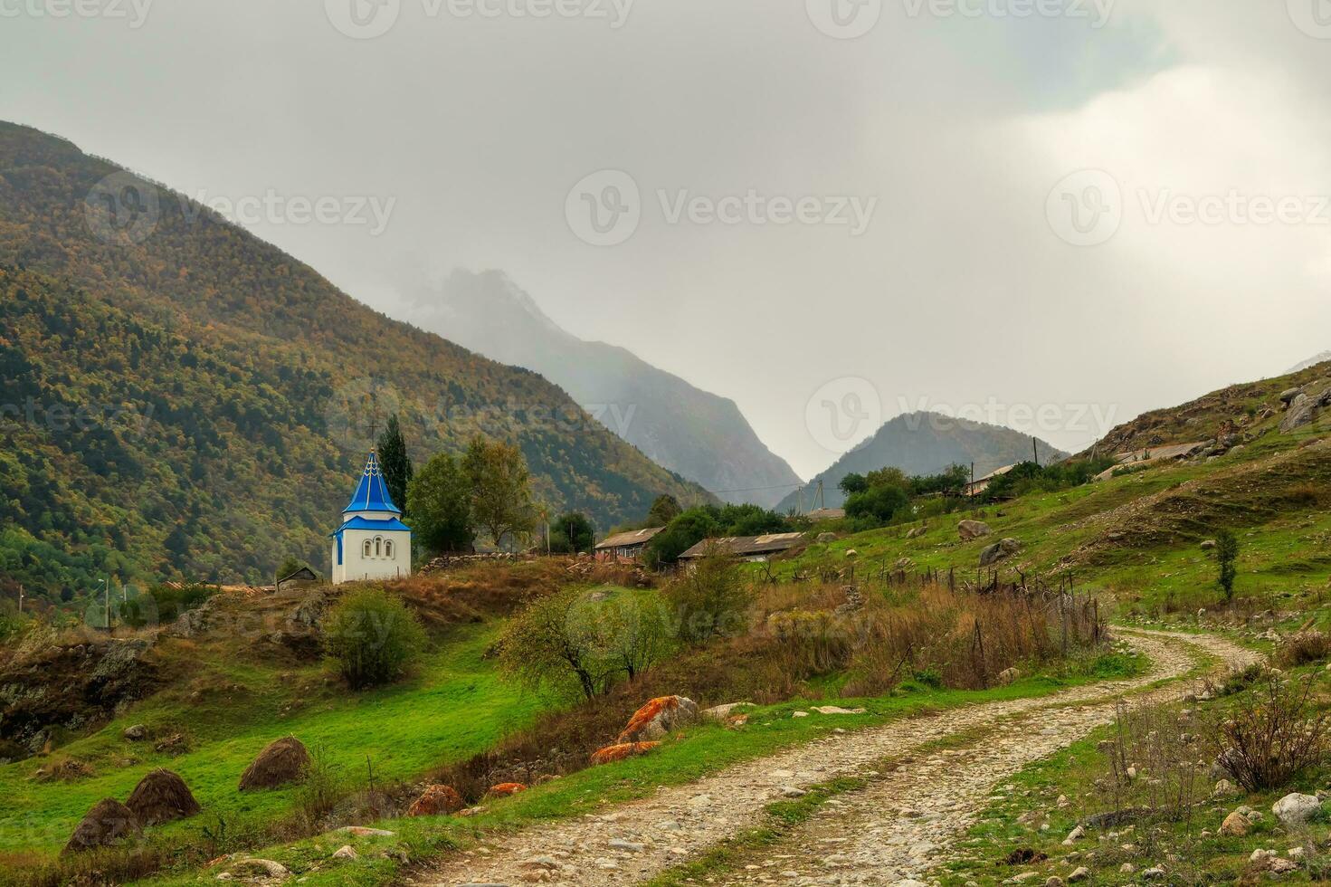 suciedad la carretera a lluvioso montañas. capilla en honor de el muerto. en honor de el icono de el madre de dios, el recuperación de el muerto capilla. irafski distrito, stur-digora aldea. Rusia. foto