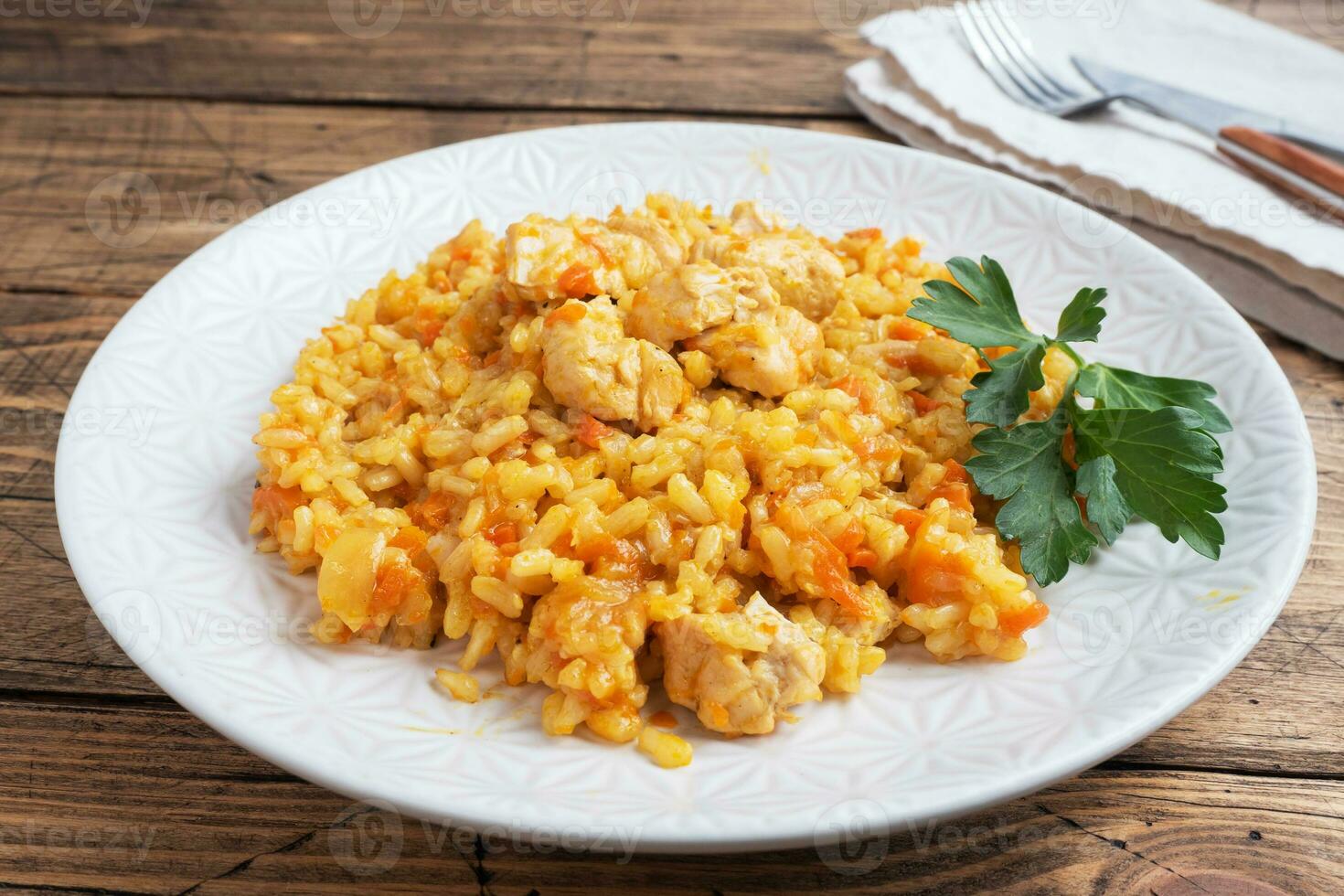Delicious Asian pilaf, stewed rice with vegetables and chicken on a plate. Wooden rustic background. photo