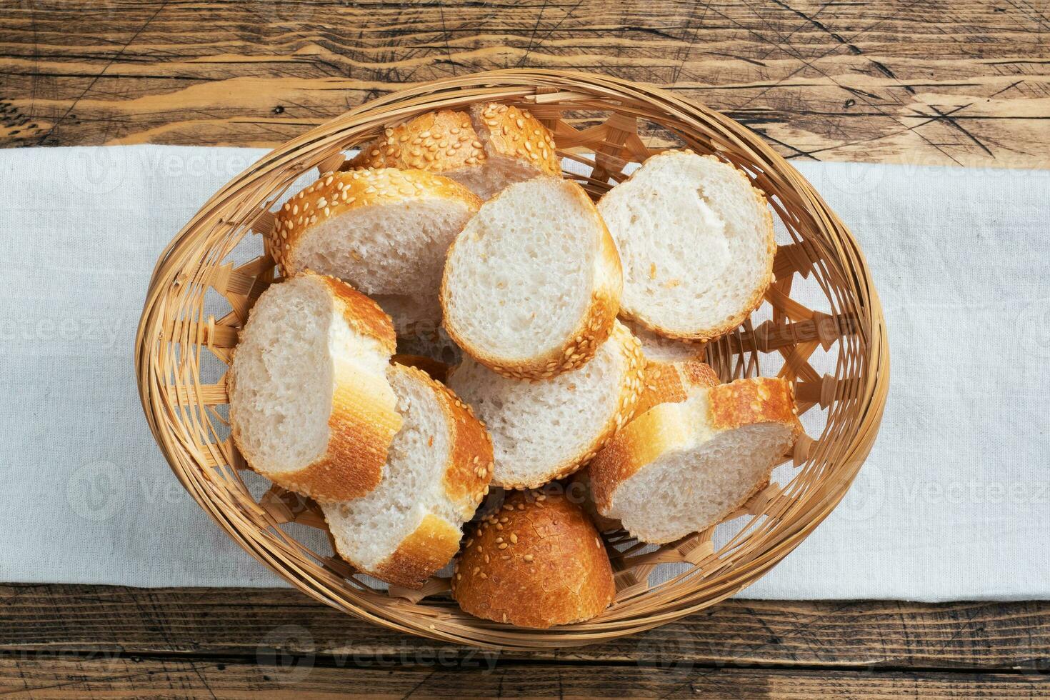 Fresh white bread, baguette slices in a wicker basket. Wooden rustic table background. Close up photo