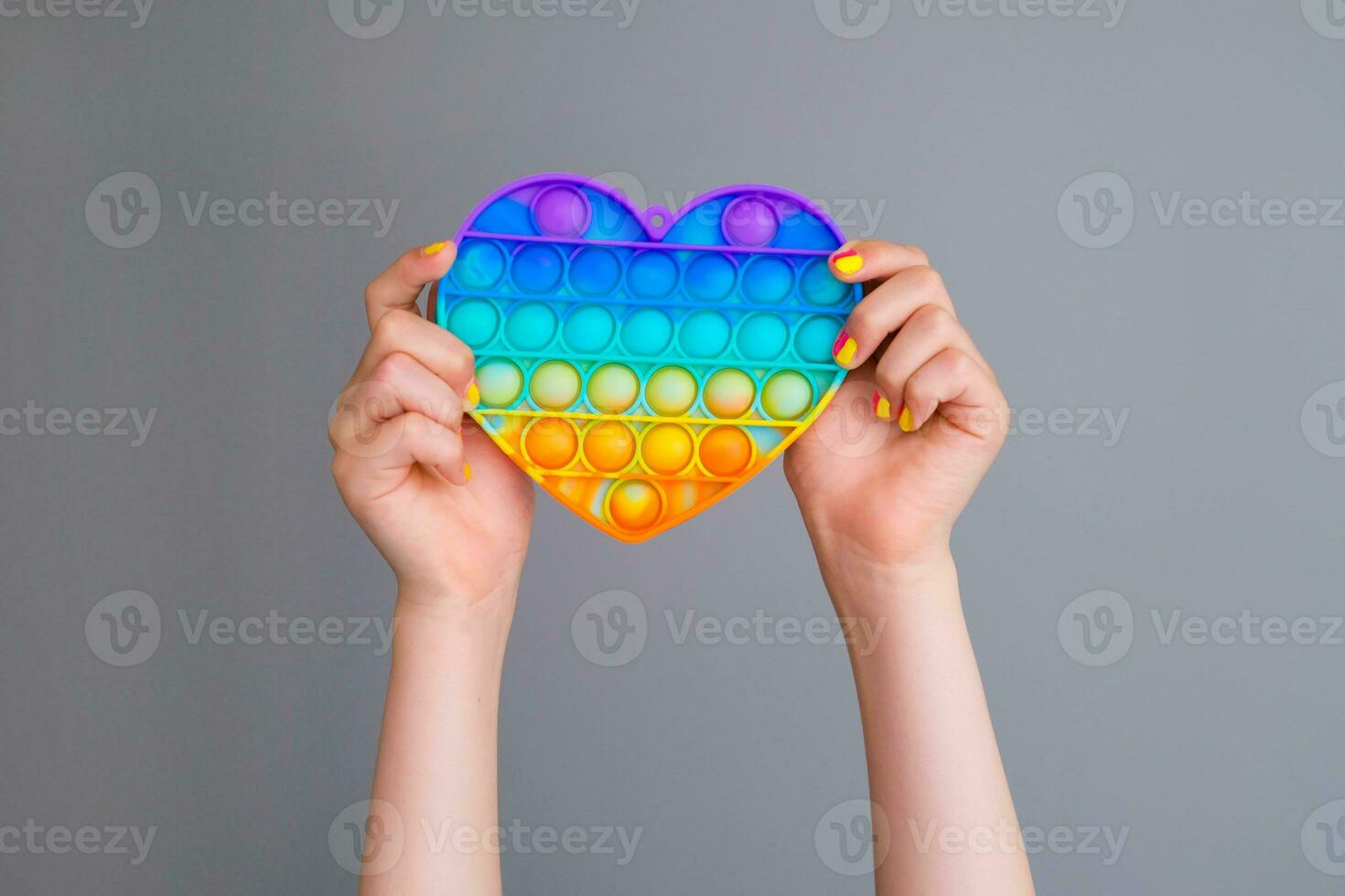 Children's hands are holding a rainbow pop it fidget toy. Push bubble fidget sensory toy - washable and reusable silicon stress relief popit. A little girl plays with an anti-stress toy takes it out . photo